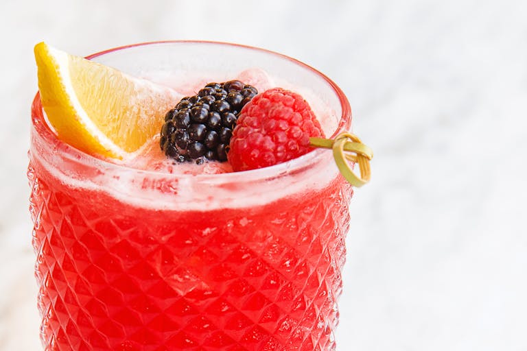 A vibrant red cocktail with berries and a lemon slice on a white background.